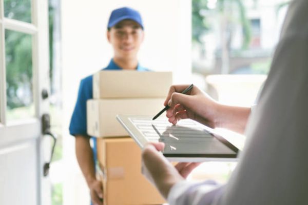 delivery, mail, people and shipping concept.Young woman sign in digital mobile phone after receiving parcel from courier at home.